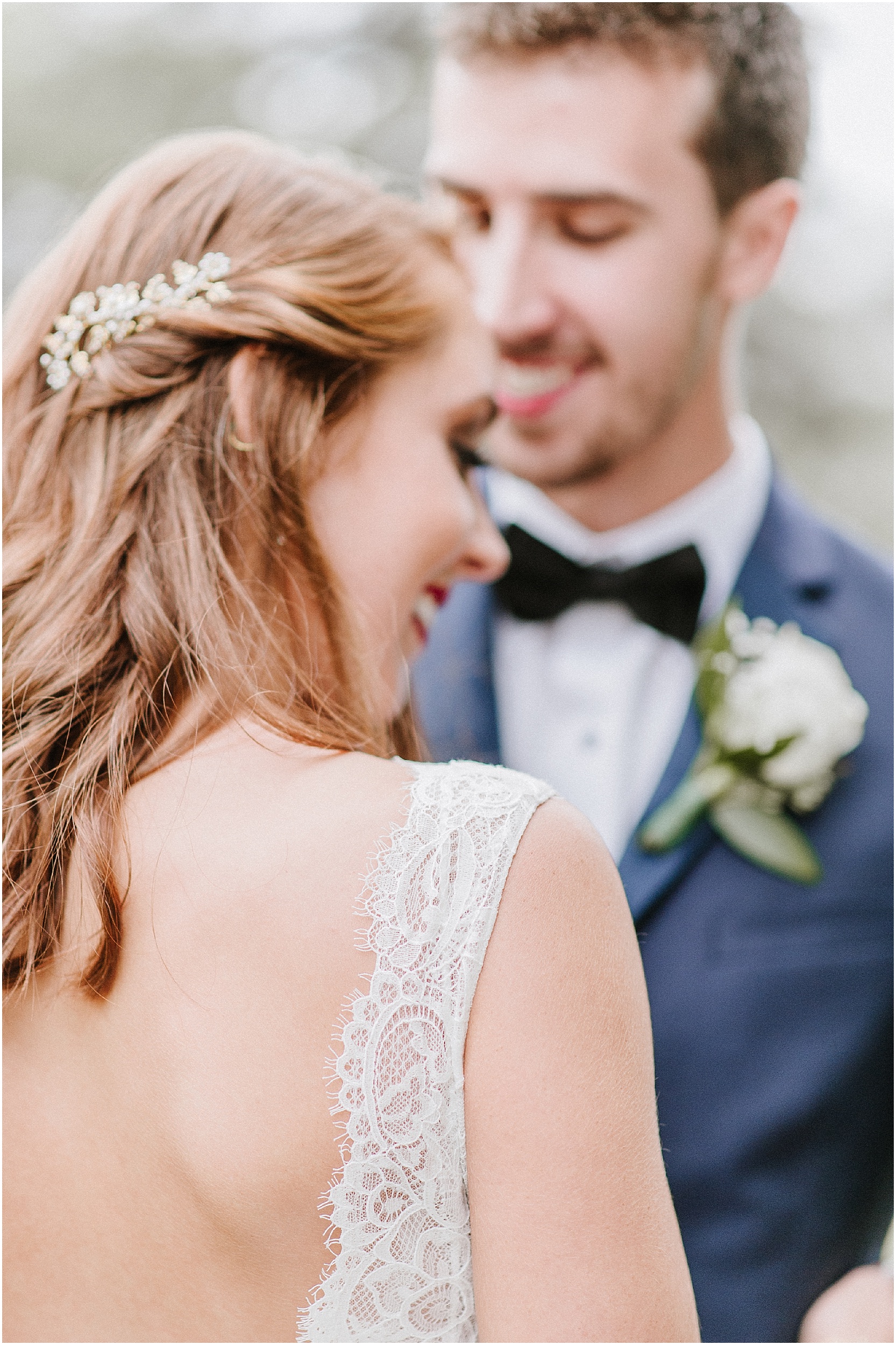 bride in lace dress with groom in blue tux smiling at her