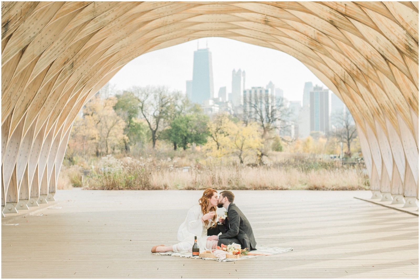 bride and groom sitting on blanket kissing beneath arch