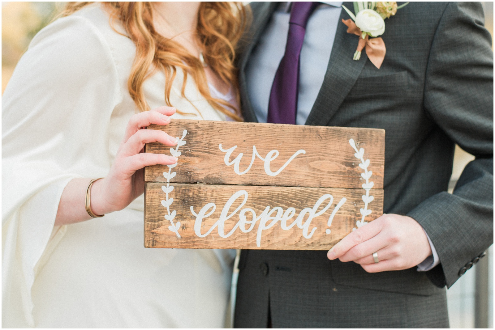 bride and groom holding a wooden we eloped sign