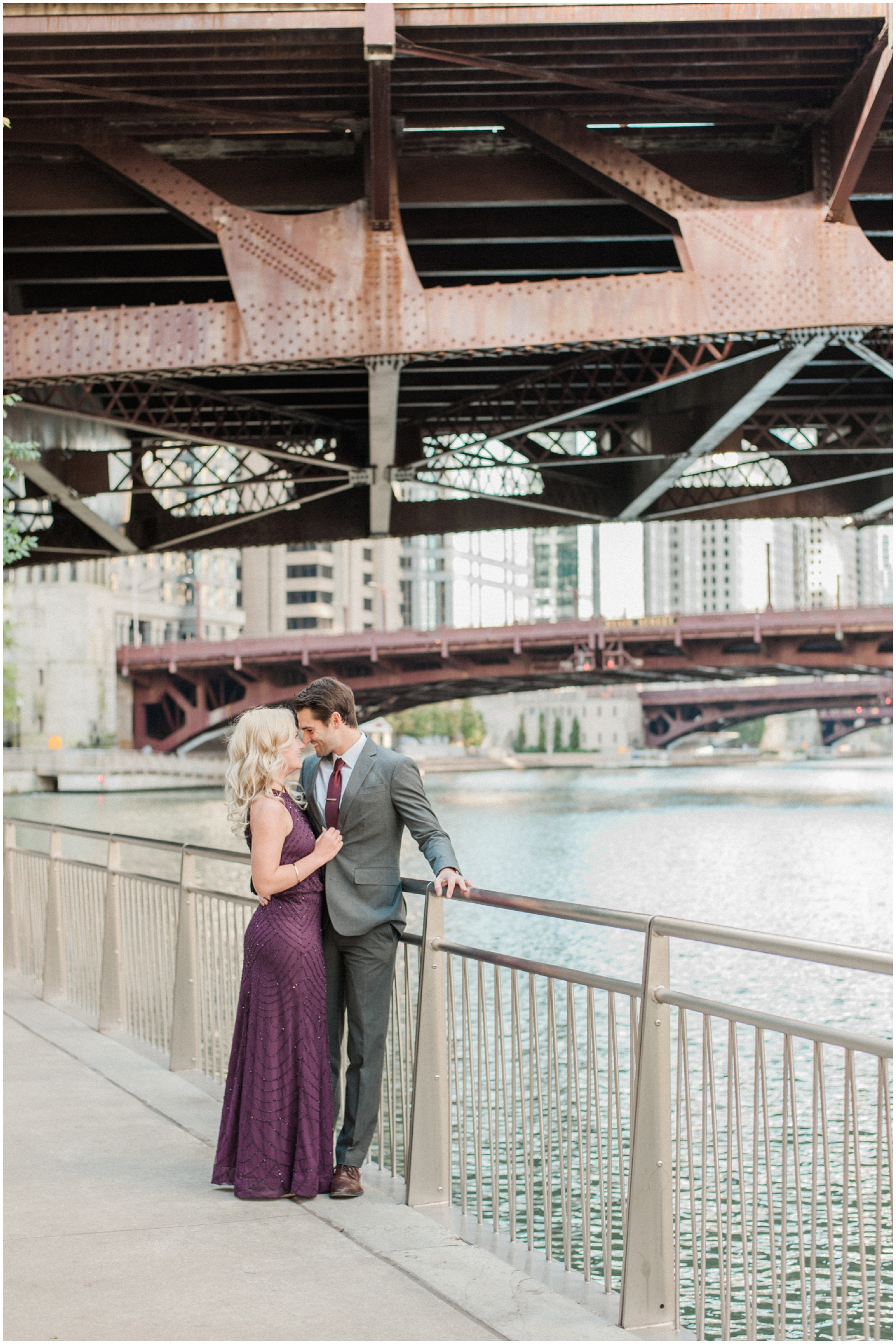 couple standing against railing alongside chicago river with bridges in background during anniversary session