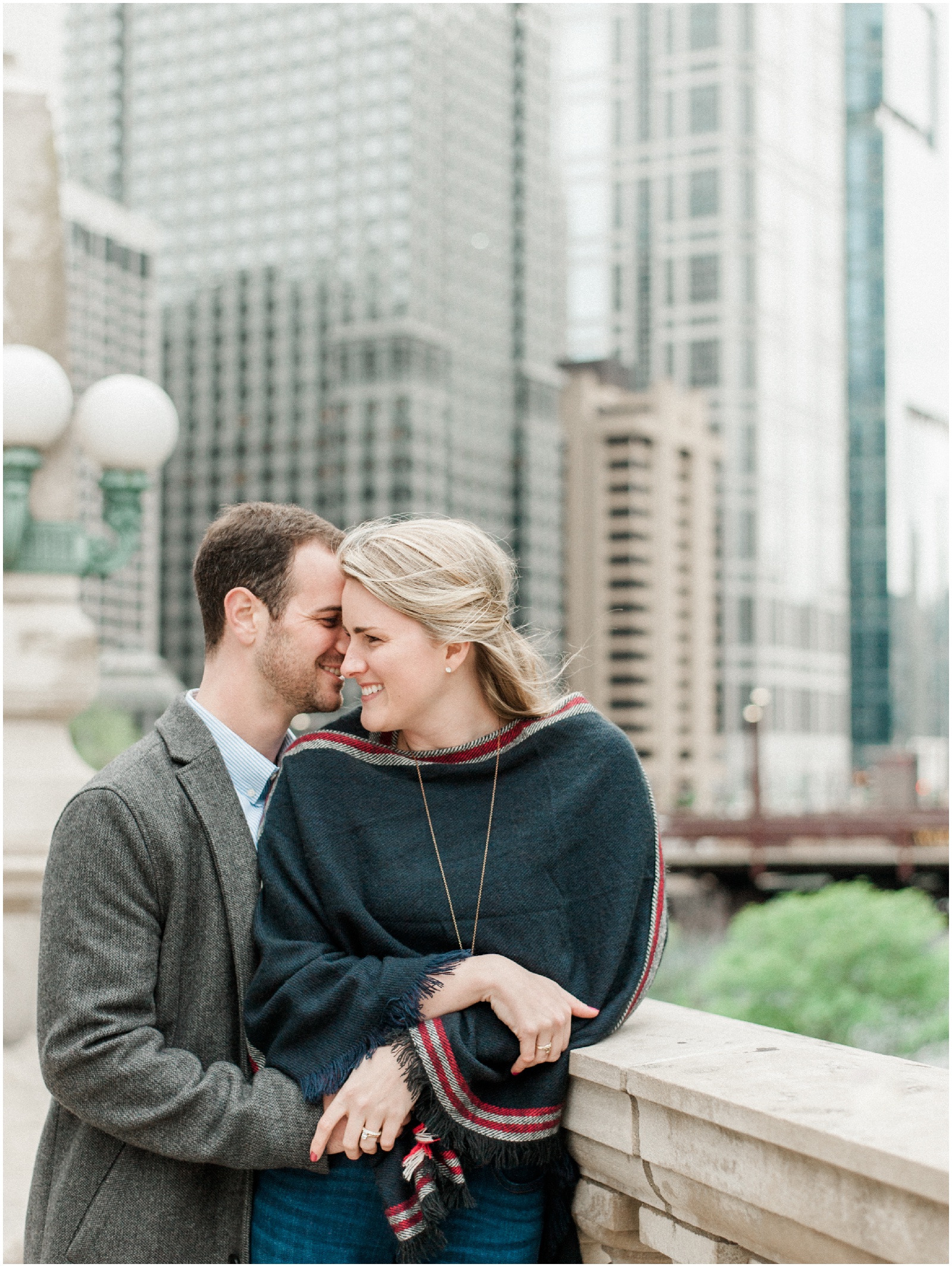 couple leaning against rail smiling at each other in front of chicago skyline during anniversary session