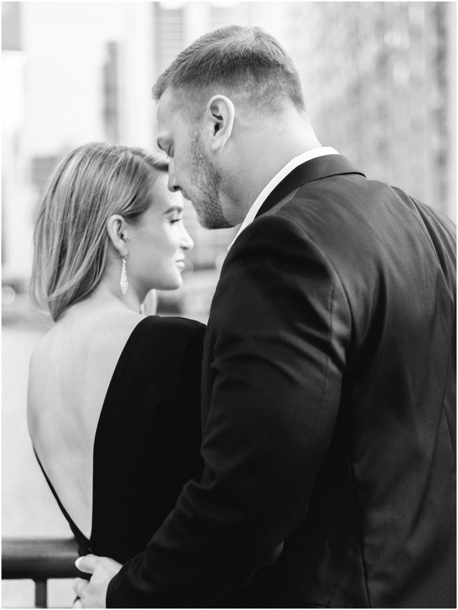 groom with hand on fiance's back wearing black and white elegant outfits