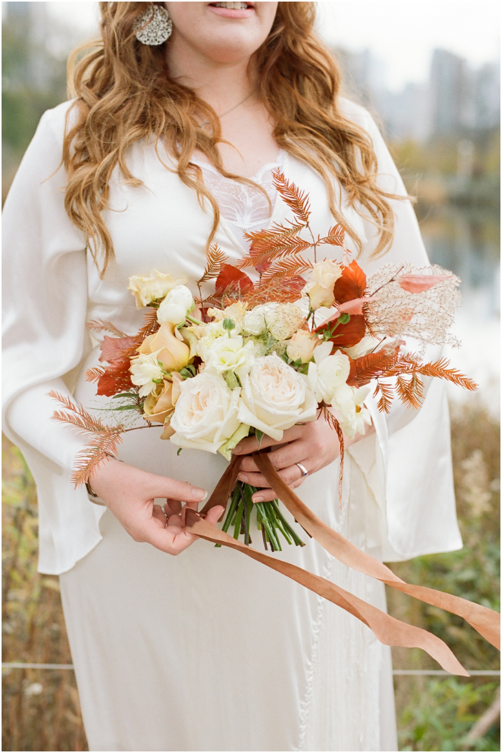 bride holding orange and cream wedding bouquet with orange leaves