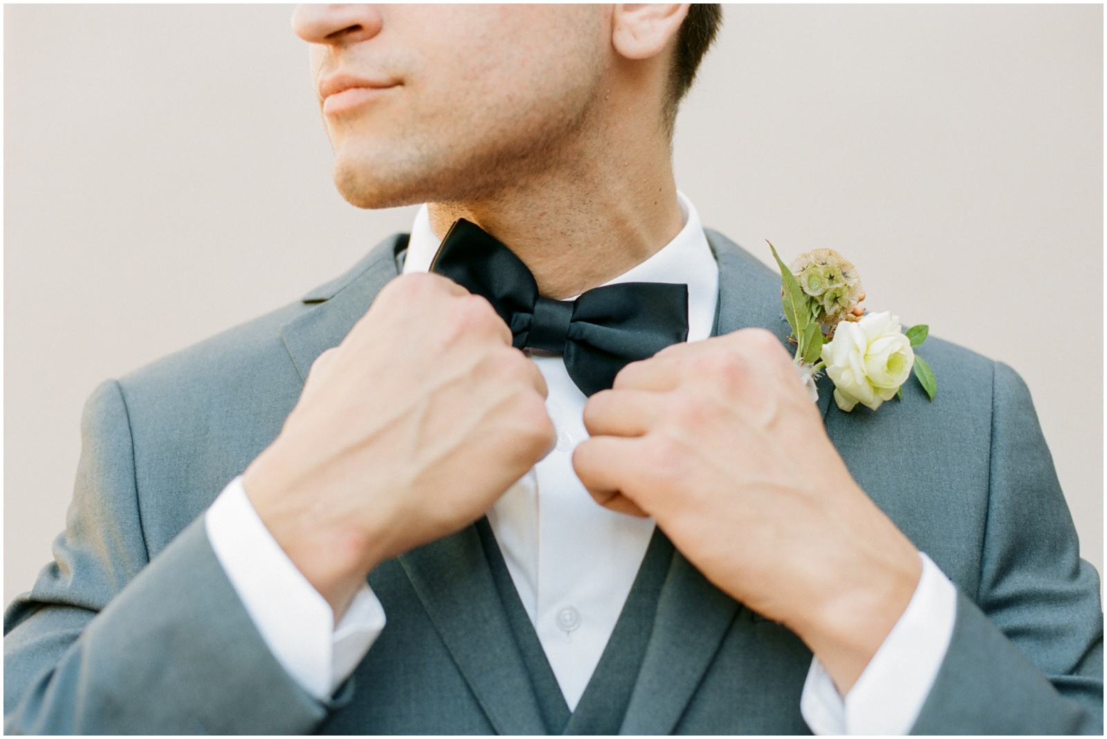 groom in grey suit adjusting black bow tie