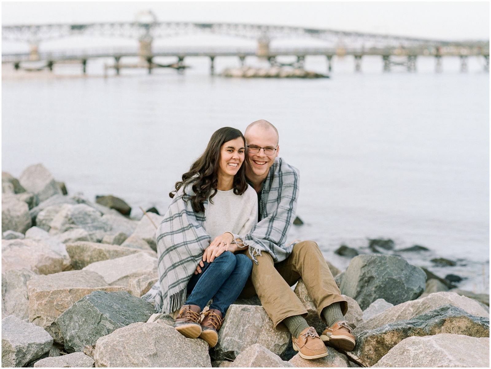 couple sitting on rocks wrapped in a blanket during engagement session