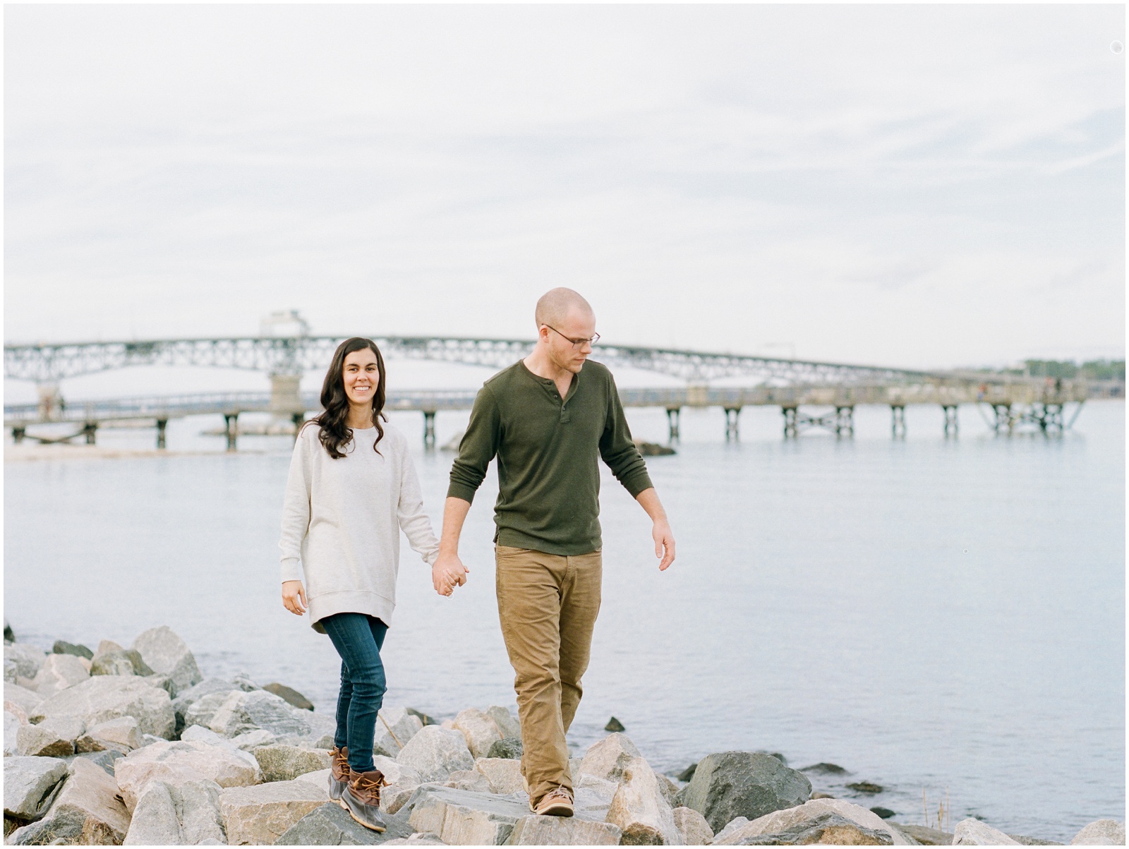 couple walking on rocks in front of river and bridge for engagement session