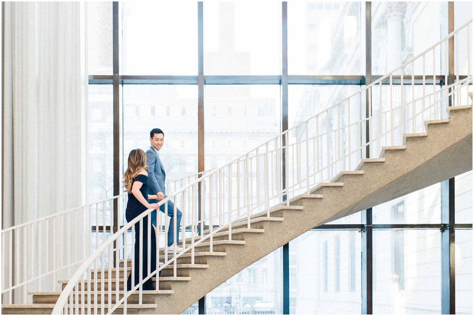couple walking up a spiral staircase in front of window during engagement session