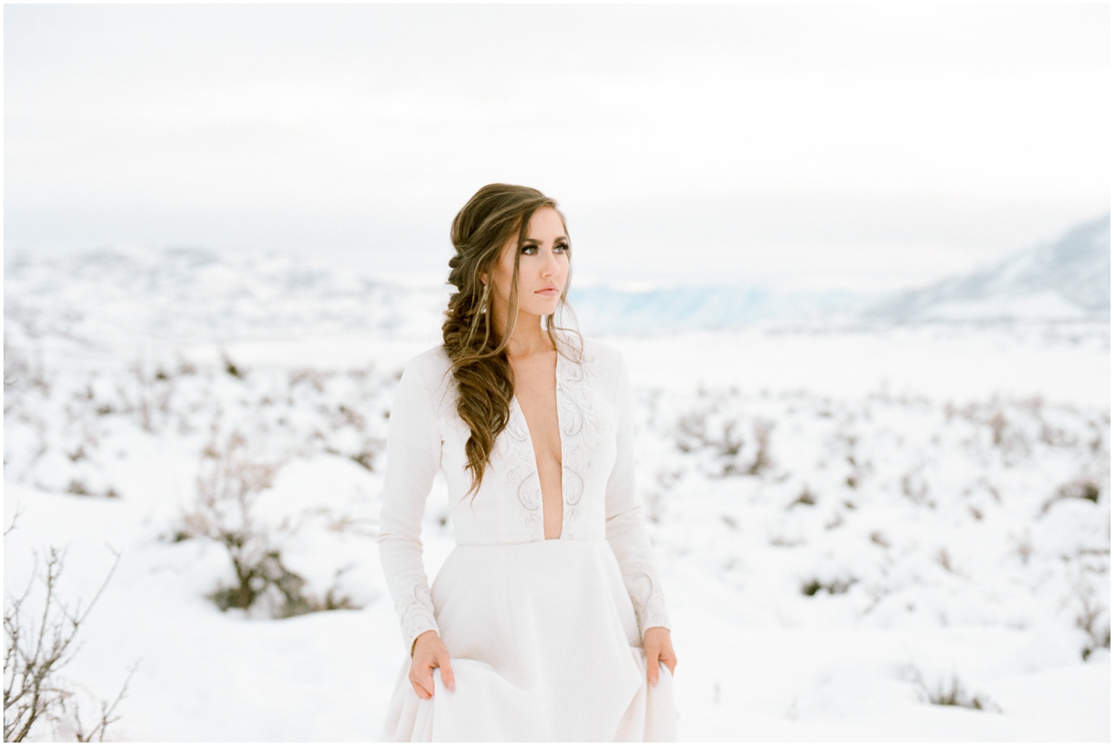 bride in chic long sleeve gown walking through snowy mountains
